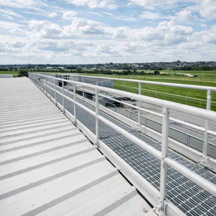Long silver safety guardrail and walkway system on a commercial roof edge.